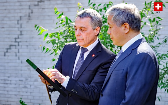 Bundesrat Ignazio Cassis und Botschafter Zhu Liying betrachten eine Urkunde. 