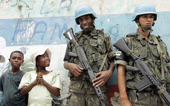 Two members of a UN armed contingent with their weapons stand next to smiling children at a demonstration of local people in Haiti