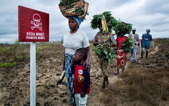 A group of women returning from work on the land pass a sign at the edge of a field warning ‘danger mines’.