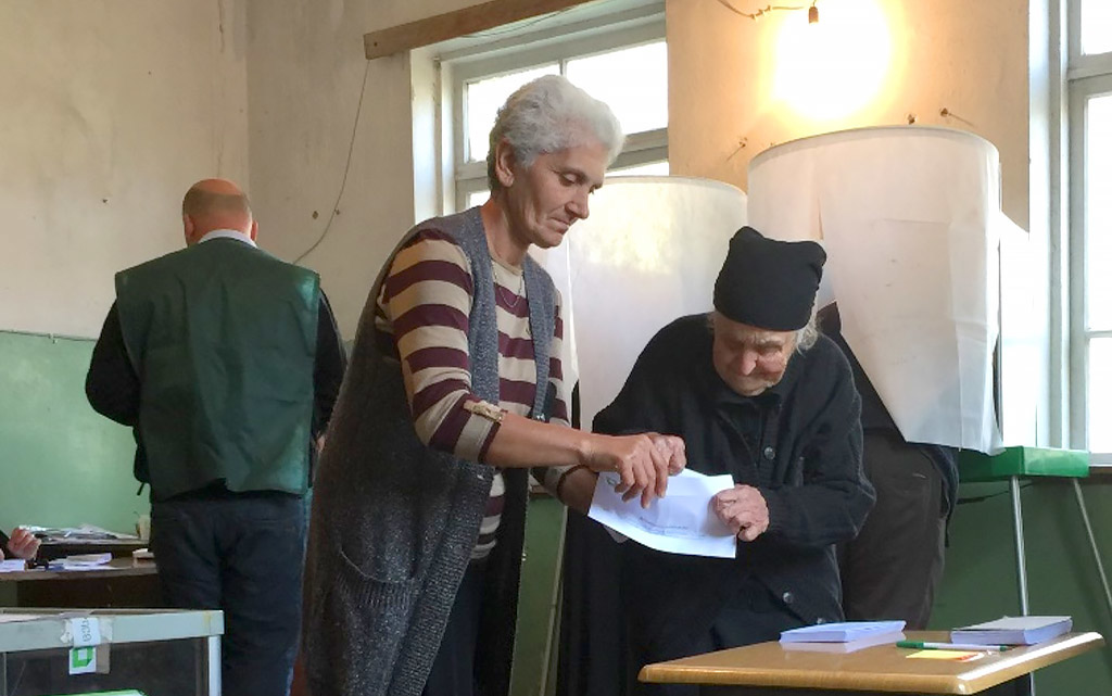 Due donne davanti a un’urna elettorale durante le elezioni locali in Georgia. Si aiutano a vicenda a piegare una scheda elettorale nel locale adibito a seggio.