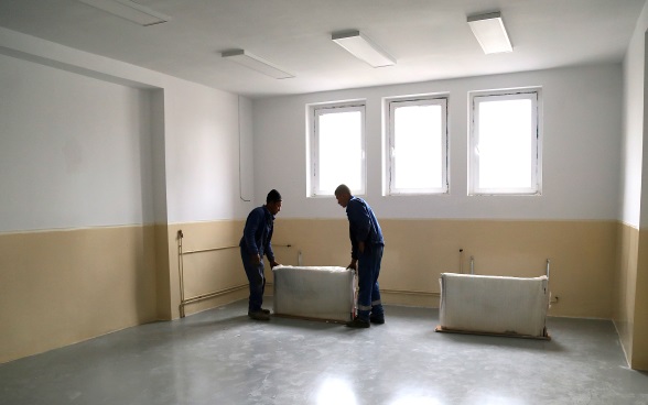 Two construction workers moving radiators into an empty classroom.