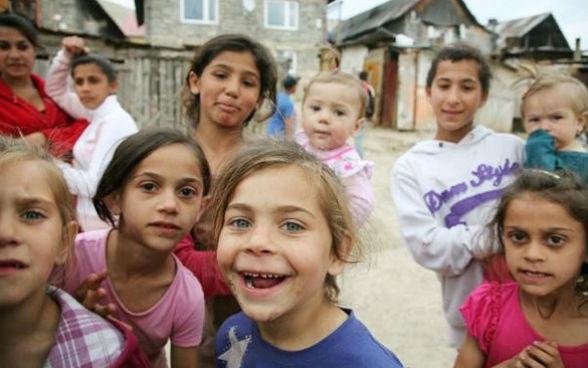 A group of nine children and a woman look into the camera.