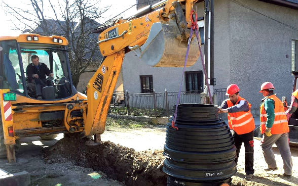 Un uomo in un’escavatrice e altri tre operai mentre posano una nuova canalizzazione.