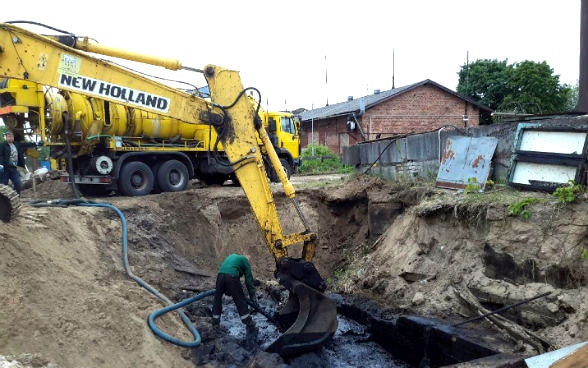 Un homme retire du sol pollué par le pétrole à l’aide d’une pelleteuse.